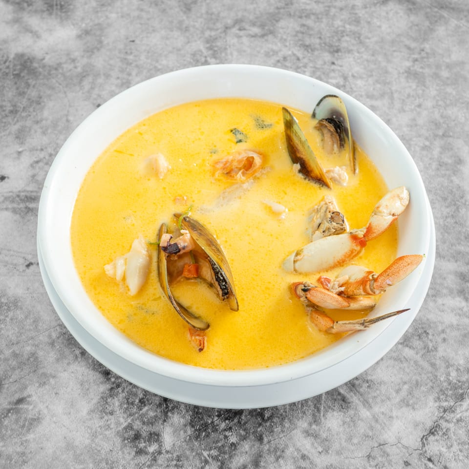 Seafood soup with mussels, crab, and shrimp in a rich yellow broth, served in a white bowl.