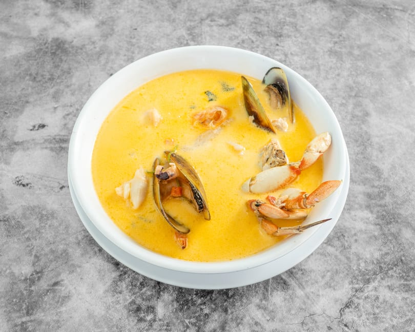 Seafood soup with mussels, crab, and shrimp in a rich yellow broth, served in a white bowl.