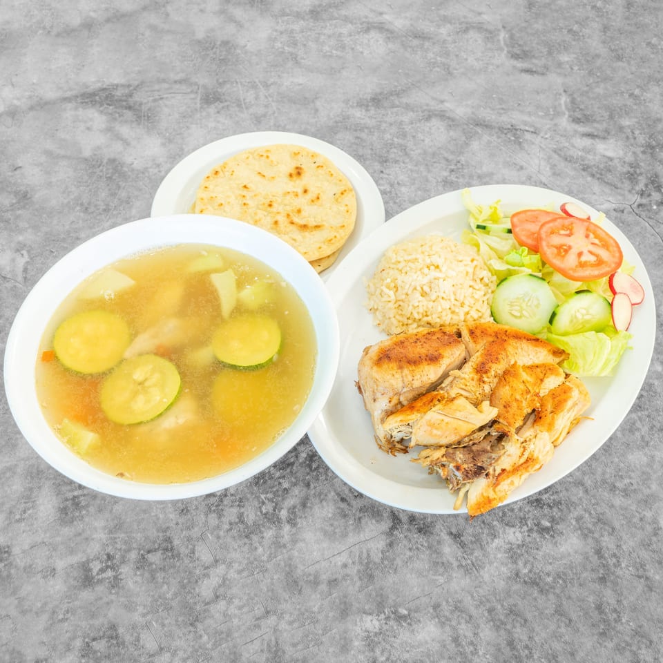 Grilled chicken with rice, salad, soup, and tortillas on a gray background.