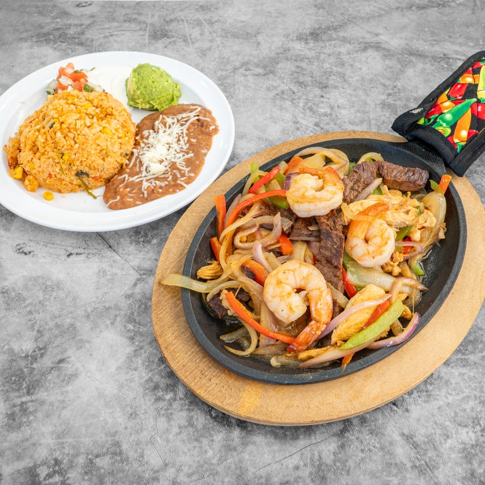 Sizzling fajitas with shrimp, steak, chicken, and vegetables, served with rice, beans, guacamole, and sour cream.
