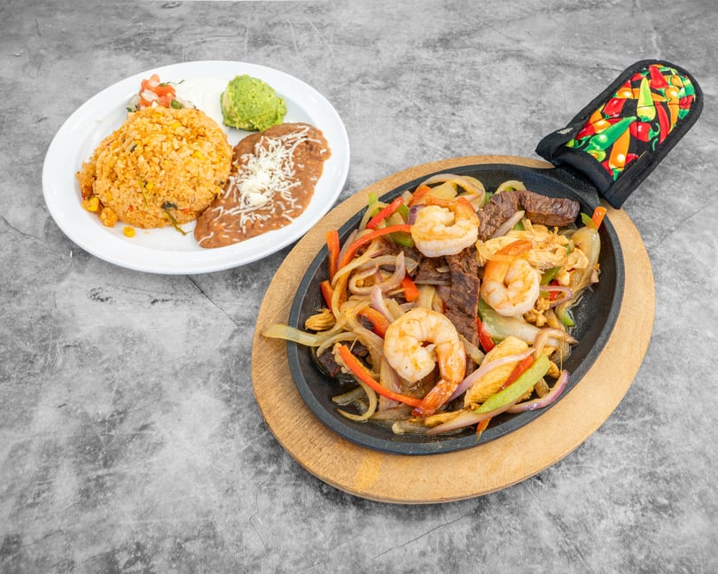 Sizzling fajitas with shrimp, steak, chicken, and vegetables, served with rice, beans, guacamole, and sour cream.