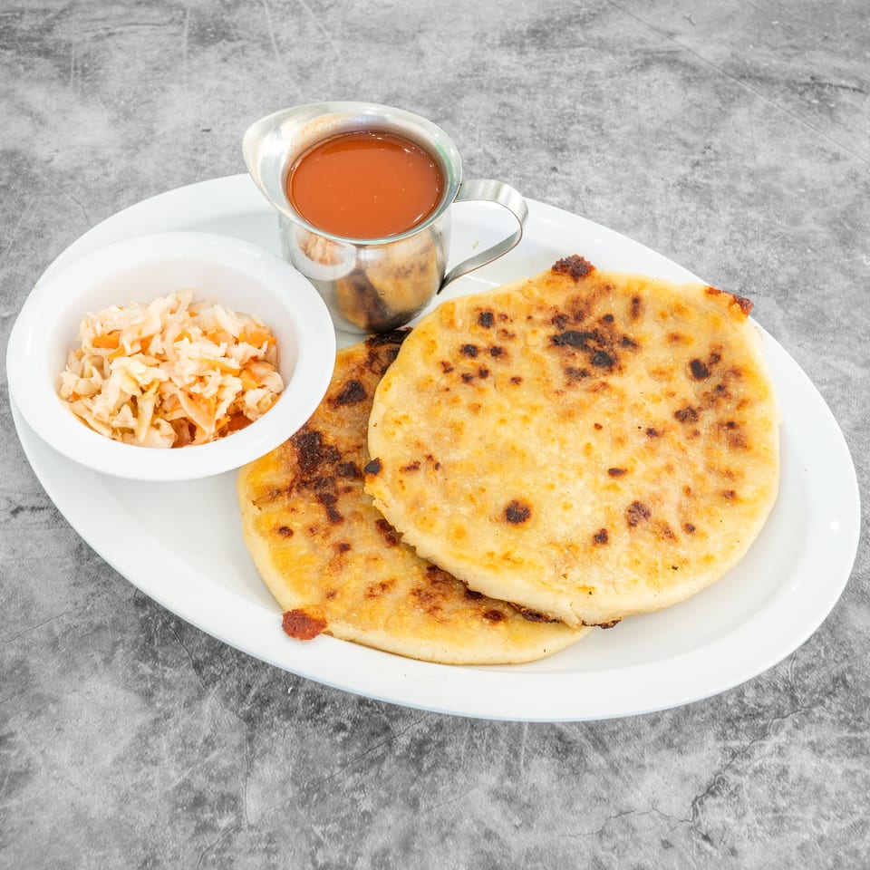 Two pupusas with curtido and red sauce on a white plate against a gray background.